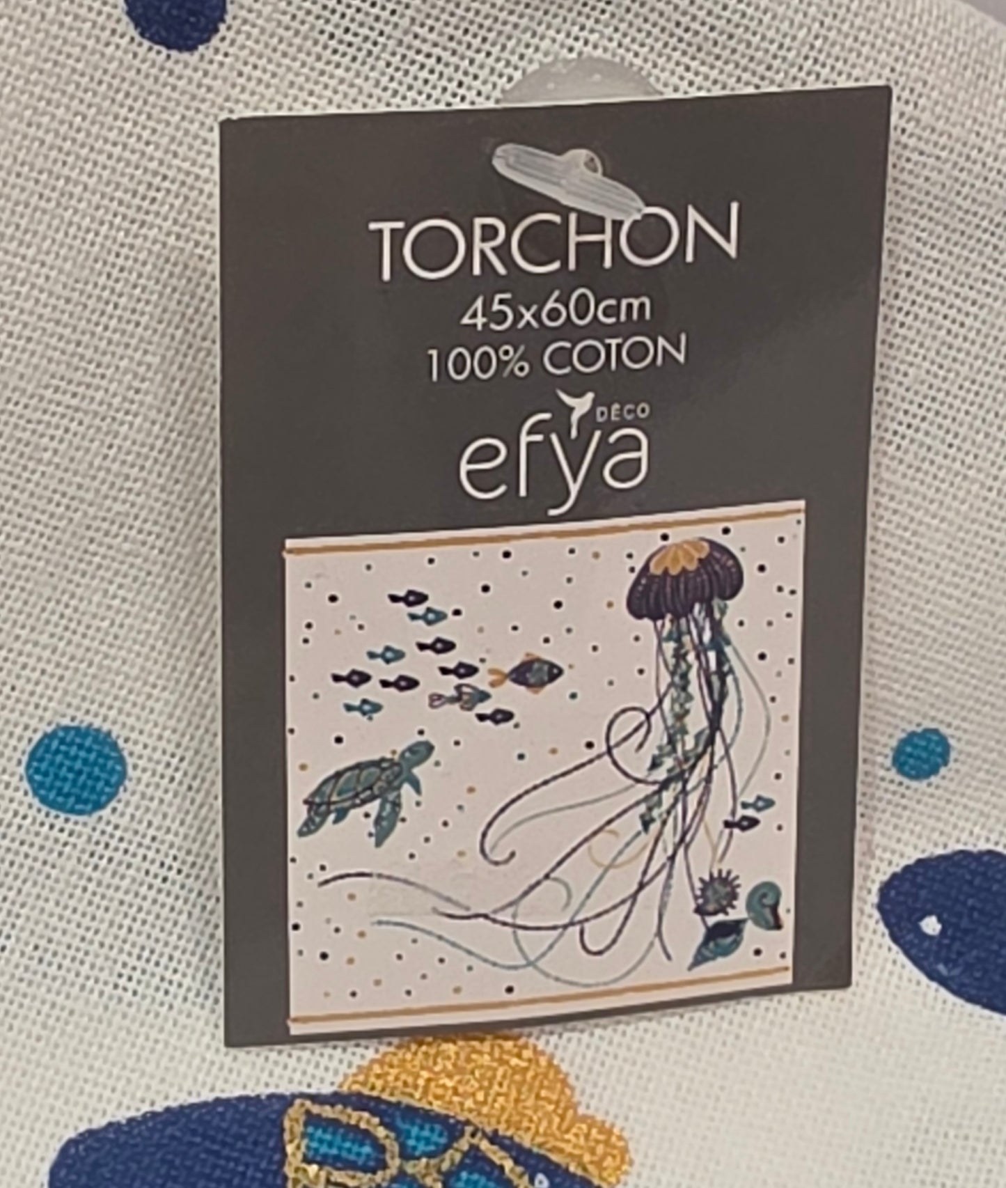 Strofinaccio da cucina in puro cotone del marchio Efya, caratterizzato da una vivace fantasia marina con pesci stilizzati e una medusa stampati nei toni del blu, azzurro e giallo ocra. Il canovaccio presenta un fondo bianco decorato da piccoli pois colorati sparsi, completato da una riga ocra sul bordo inferiore e da una pratica asola scura per appenderlo.