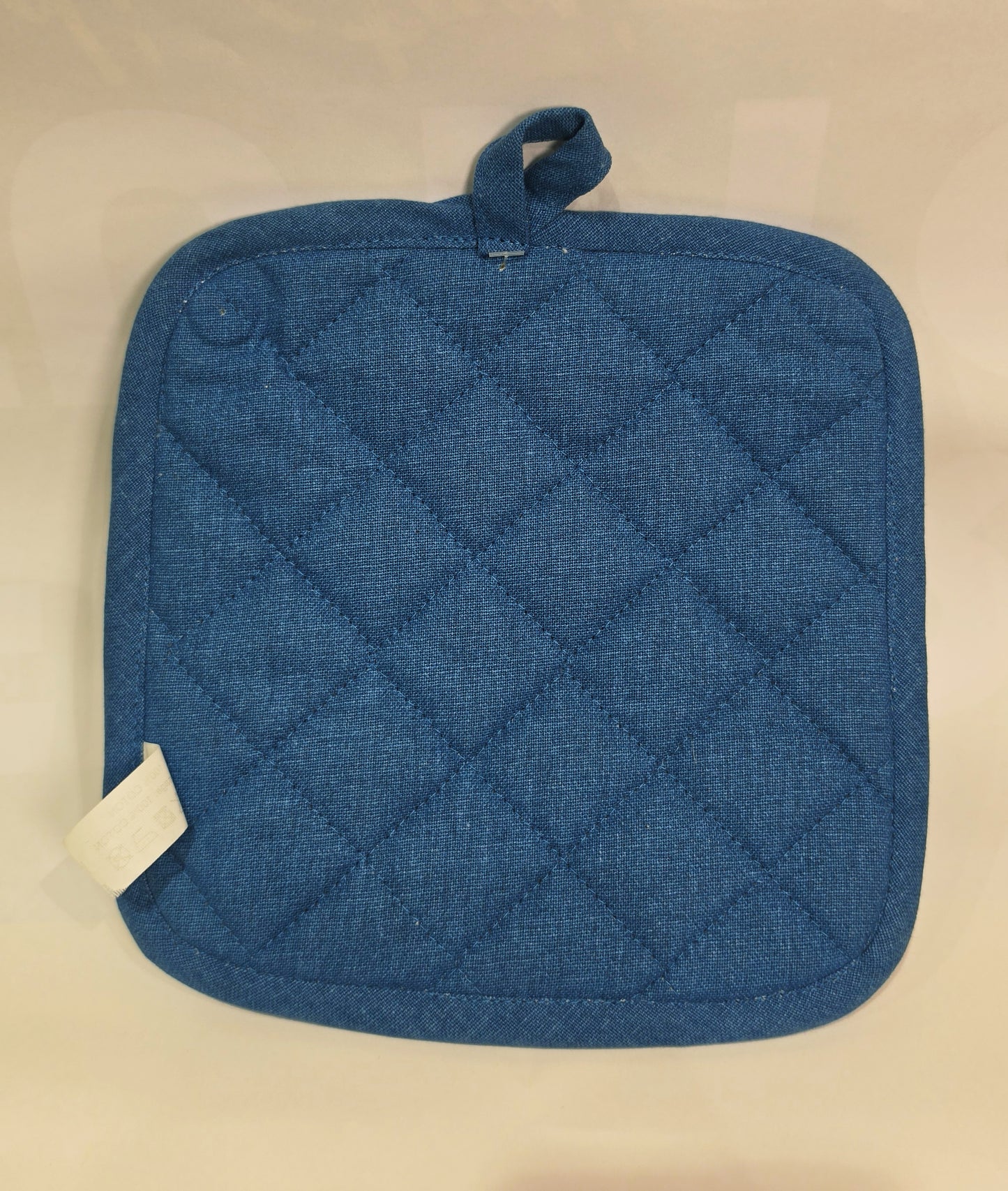 Presina da cucina quadrata in cotone caratterizzata da una fantasia a tema marino con pesciolini stampati in varie tonalità di blu, azzurro e dettagli ocra. Il tessile presenta uno sfondo a righe verticali sfumate, un bordo perimetrale blu e una pratica asola superiore per appenderla comodamente in cucina.