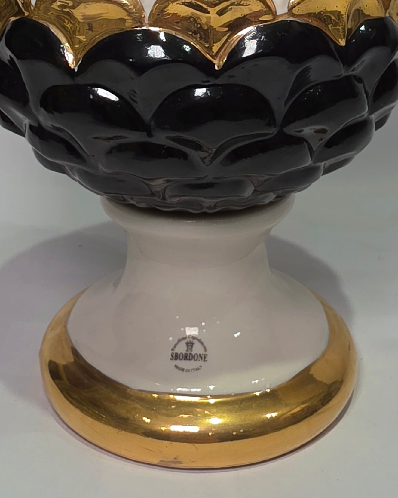 Pigna portafortuna in ceramica artigianale bicolore bianca e nera lucida, caratterizzata da una fascia centrale dorata che separa le squame in rilievo. Questo elegante oggetto ornamentale con base d'appoggio rifinita in oro è un complemento d'arredo di design ideale per donare un tocco di prestigio e tradizione siciliana agli ambienti contemporanei.