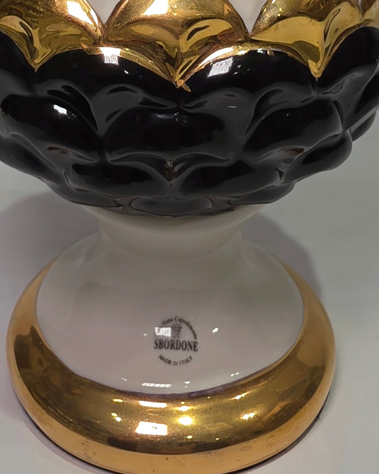 Pigna portafortuna in ceramica artigianale bicolore bianca e nera lucida, caratterizzata da una fascia centrale dorata che separa le squame in rilievo. Questo elegante oggetto ornamentale con base d'appoggio rifinita in oro è un complemento d'arredo di design ideale per donare un tocco di prestigio e tradizione siciliana agli ambienti contemporanei.