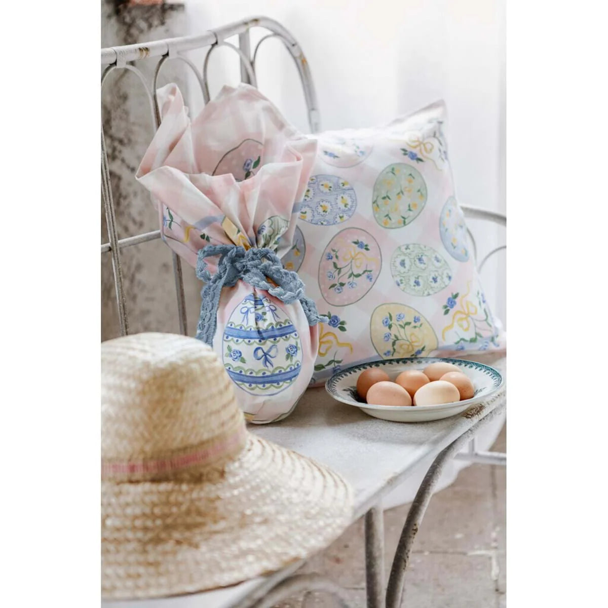 Foulard centrotavola della collezione "Pretty Easter" avvolto a forma di uovo di Pasqua e chiuso da un nastro bianco logato. Il tessuto presenta una delicata fantasia a scacchi bianchi e rosa confetto impreziosita da illustrazioni di uova pasquali decorate con roselline azzurre e fiocchi, ideale per arricchire la tavola primaverile in perfetto stile shabby chic.