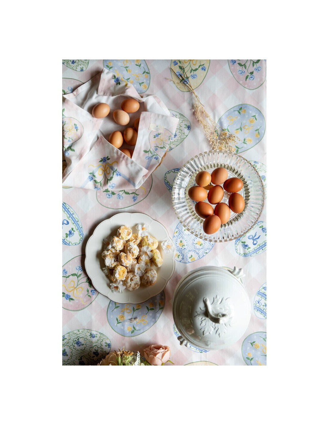 Tovaglia rettangolare della collezione "Pretty Easter" caratterizzata da una base a scacchi bianchi e rosa confetto con una balza in tinta unita sul bordo inferiore. Il tessuto è interamente stampato con uova di Pasqua decorate da motivi floreali, fiocchi gialli e trame geometriche nei toni del pastello, perfetta per apparecchiare la tavola festiva in stile shabby chic.
