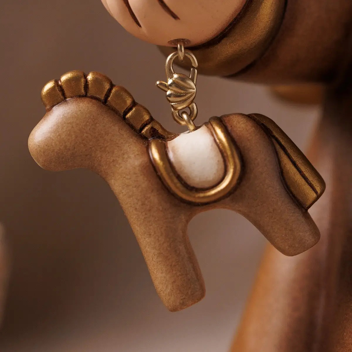 Statuetta in ceramica Thun in edizione limitata raffigurante l'Angelo del Centenario con veste marrone e finiture dorate, che regge un piccolo cavallino a dondolo dorato.