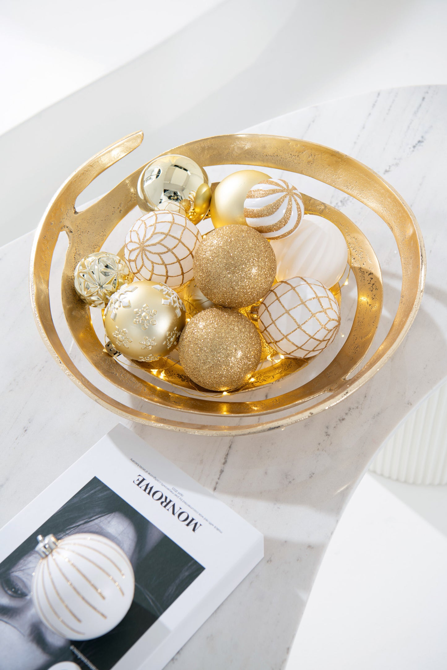 La ciotola dorata utilizzata come centrotavola su un piano di marmo, riempita con palline di Natale bianche e oro di diverse texture.