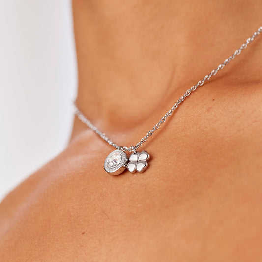 Primo piano della collana Lucky Light indossata. La catena d'acciaio poggia delicatamente sul décolleté, mettendo in risalto i pendenti con cristallo circolare e il quadrifoglio in acciaio lucido.
