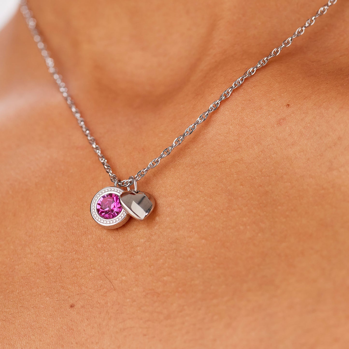 Primo piano della collana Lucky Light indossata. La catena d'acciaio poggia delicatamente sul décolleté, mettendo in risalto i pendenti con cristallo fucsia e il cuore in acciaio lucido.
