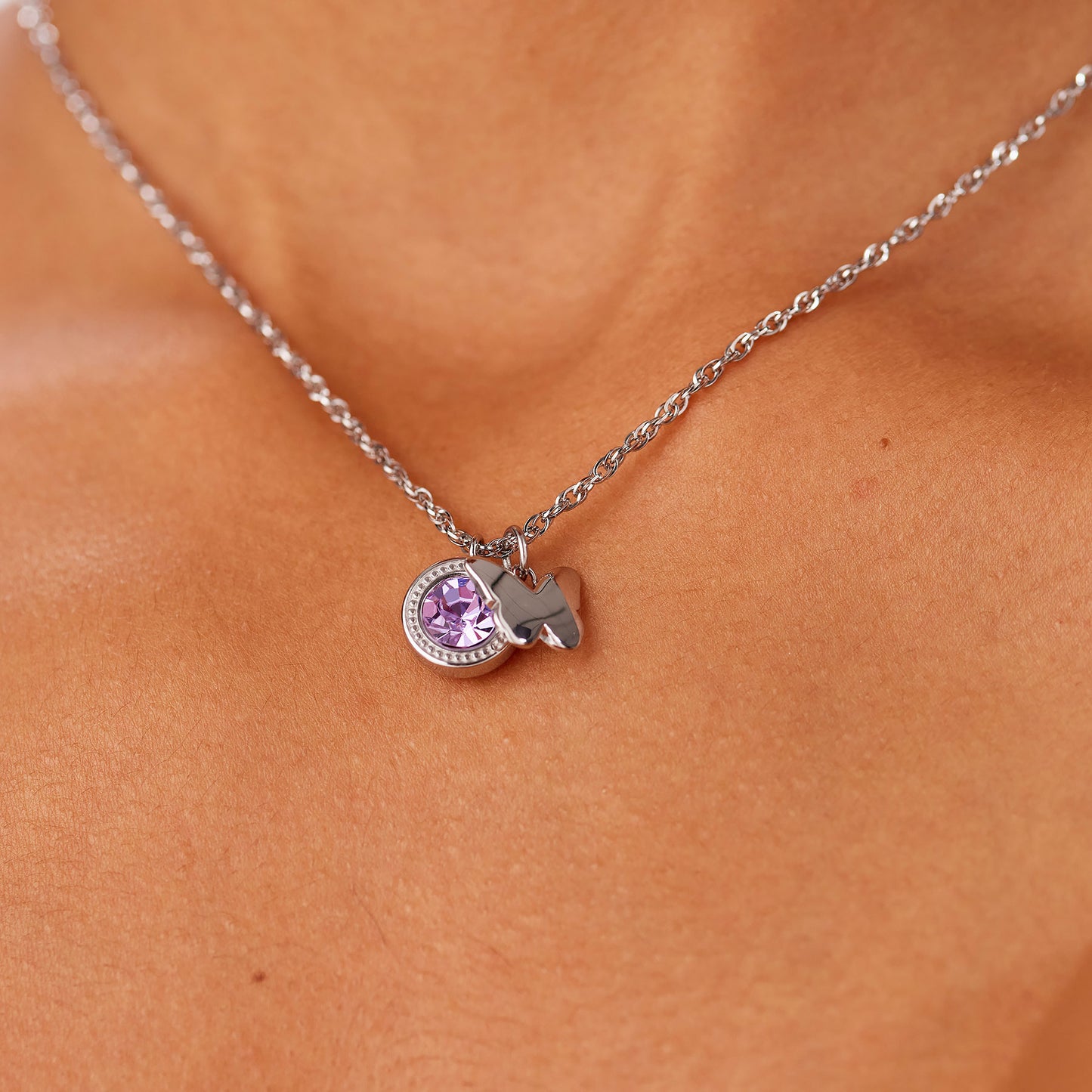 Primo piano della collana Lucky Light indossata. La catena d'acciaio poggia delicatamente sul décolleté, mettendo in risalto i pendenti con cristallo viola e la farfalla in acciaio lucido.
