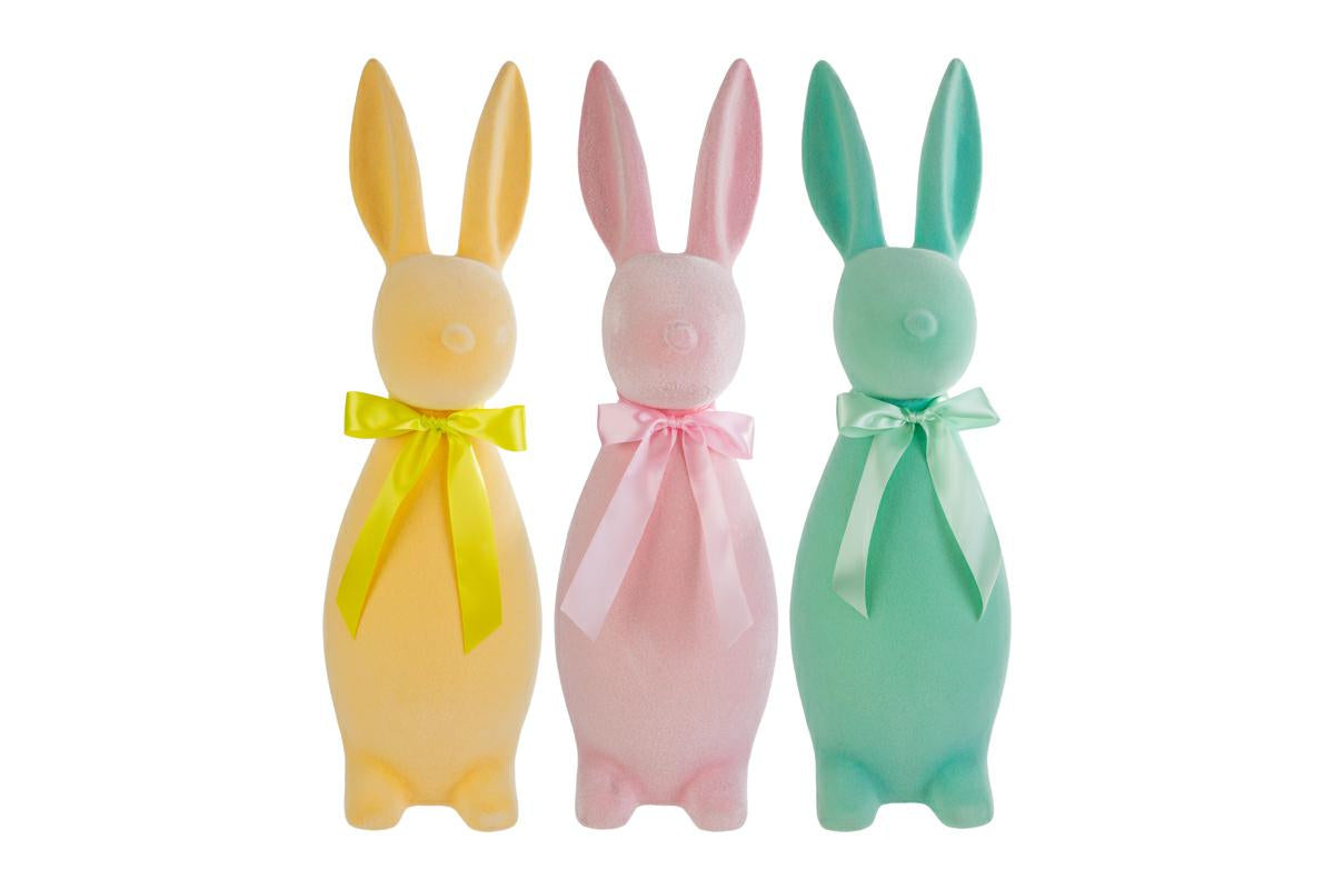 Tris di coniglietti pasquali decorativi del marchio Le Stelle (codice 12224) con finitura floccata effetto velluto. Il set comprende tre varianti di colore pastello: giallo ocra, rosa cipria e verde acqua, ognuna ornata da un fiocco in raso coordinato. Statuine dal design stilizzato e moderno per l'arredamento di Pasqua.