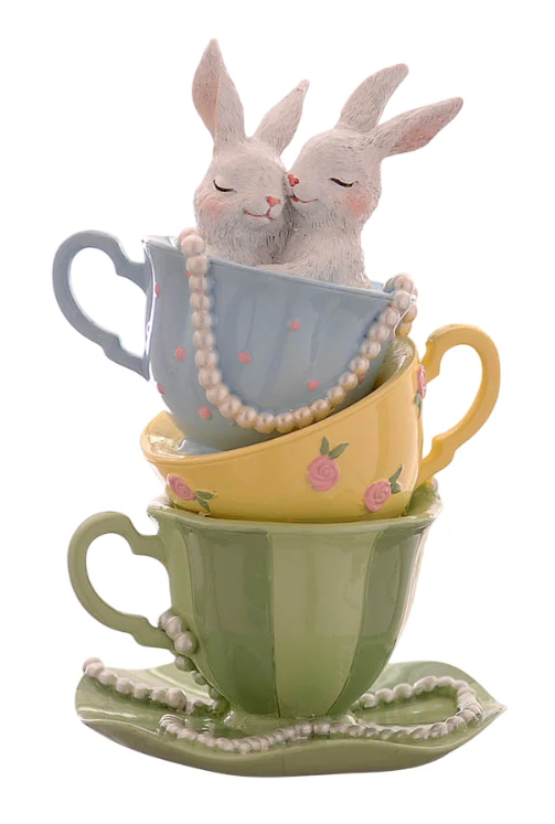 Statuina decorativa in resina che raffigura due coniglietti bianchi abbracciati, con gli occhi chiusi, che spuntano da una tazzina azzurra a pois rosa. La tazzina è impilata sopra una tazzina gialla decorata con rose rosa e una tazzina verde a strisce scure. Una lunga collana di perle bianche decora la composizione, partendo dall'interno della tazzina superiore e avvolgendosi attorno alla base verde.