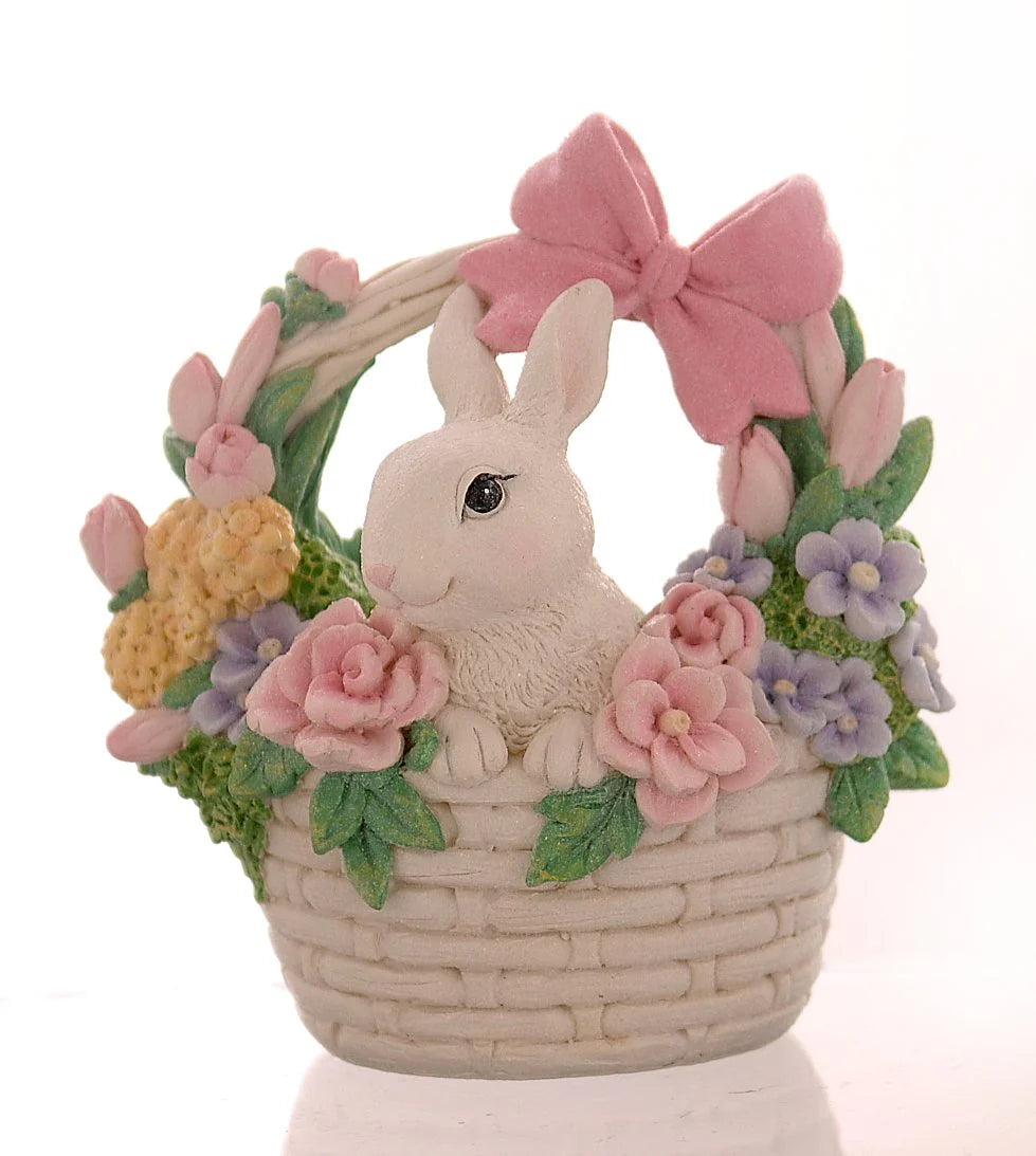 Decorazione pasquale scultorea Vetur in poliresina. Coniglietto bianco che spunta da un cestino intrecciato bianco, decorato con un grande fiocco rosa sul manico e circondato da una ghirlanda di rose rosa, fiori viola e tulipani.