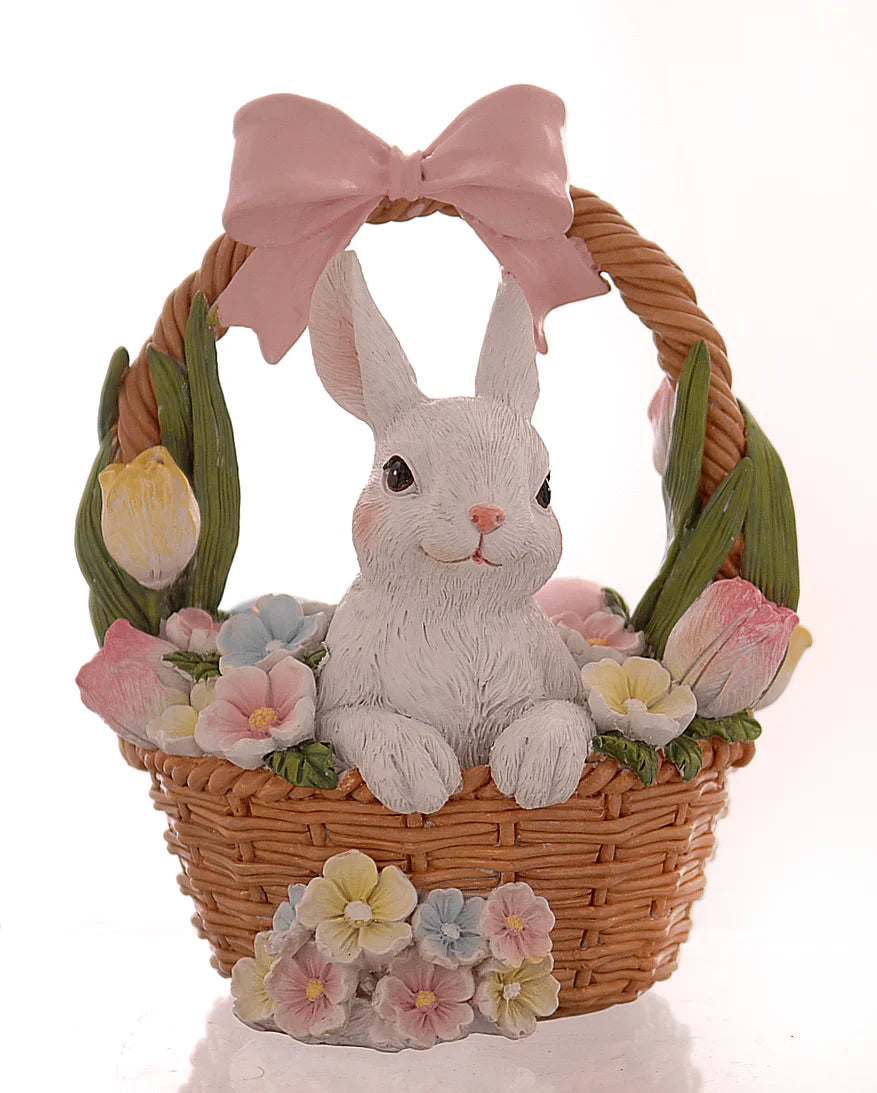 Decorazione pasquale Vetur in poliresina. Coniglietto bianco seduto all'interno di un cestino di vimini intrecciato, circondato da tulipani e fiori primaverili pastello, con un grande fiocco rosa sul manico.