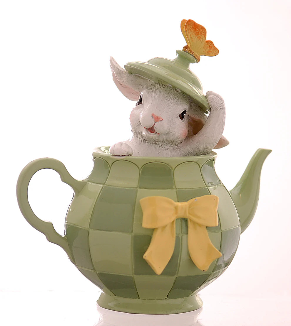 Decorazione pasquale Vetur in poliresina. Coniglietto bianco che fa capolino da una teiera verde con motivo a scacchi, decorata con un fiocco giallo e una farfalla arancione sul coperchio sollevato.