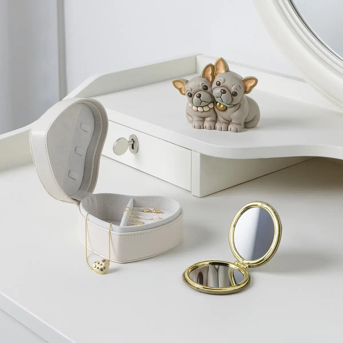 L'immagine presenta la statuetta dei Bulldog Francesi posizionata su un mobile da toeletta bianco, circondata da accessori femminili e raffinati che ne suggeriscono l'uso come oggetto da regalo o elemento decorativo per la camera da letto.