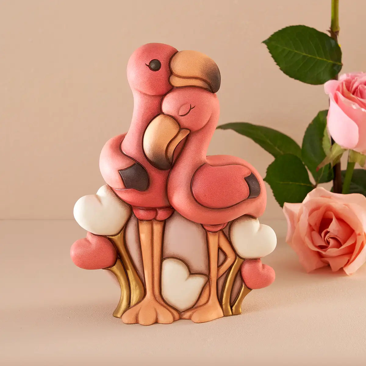 Coppia di fenicotteri maxi THUN in ceramica rosa esposta su un piano neutro accanto a rose rosa, mostrandone le proporzioni e l'uso come complemento d'arredo elegante.