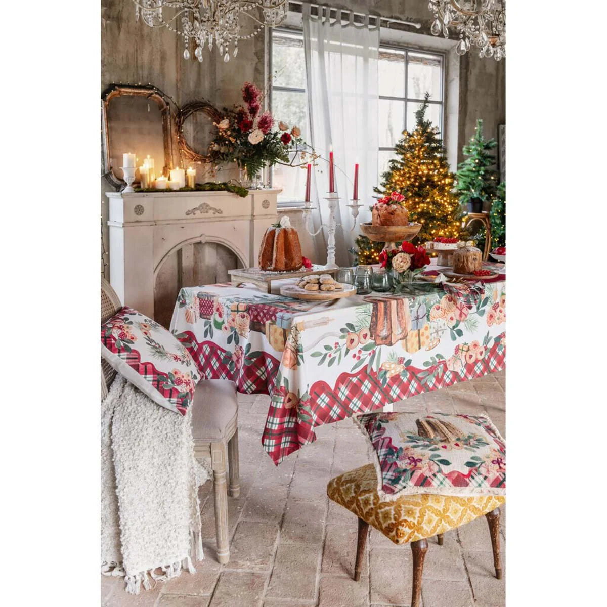 Tavola natalizia Blanc Mariclo con tovaglia coordinata, pandoro e dolci. In primo piano, due cuscini decorativi su sedie diverse, circondati da un'atmosfera calda con alberi di Natale illuminati.