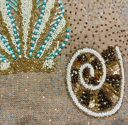 dettaglio del cuscino Blanc Mariclo' linea Maldive in lino naturale color beige. Stampa marina con conchiglie ricamate sabbia e azzurro. Complemento d'arredo per case estive.