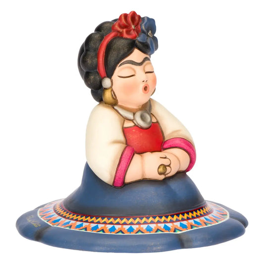 Statuina in ceramica Thun della collezione Frida Kahlo in formato medio, ritratta in una posa iconica con occhi chiusi e labbra socchiuse. La figura indossa abiti tradizionali messicani, tra cui una gonna blu decorata con motivi geometrici etnici e fiori colorati tra i capelli neri, rappresentando un pezzo da collezione ricco di fascino e significato culturale.