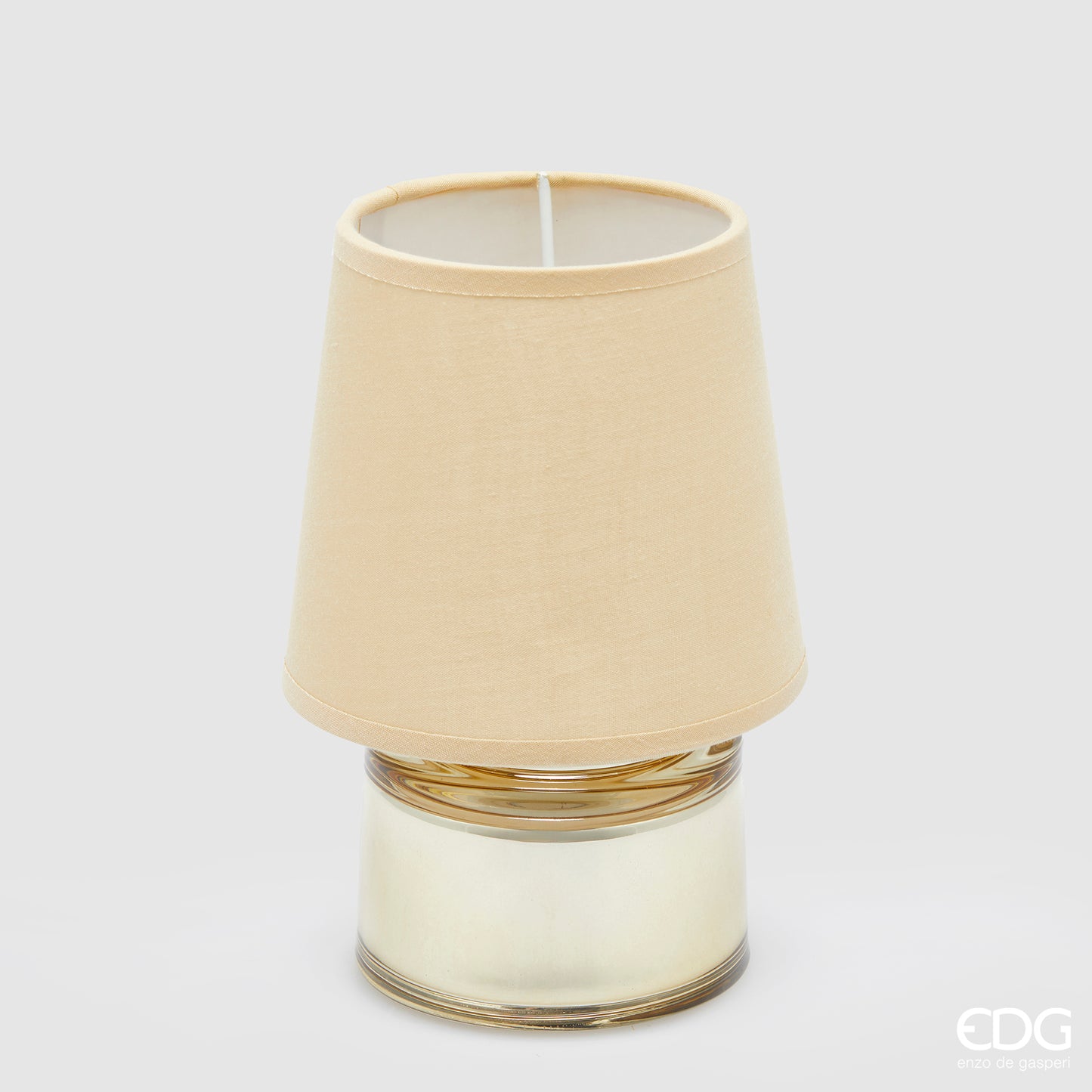 Piccola lampada da tavolo EDG Cozy color crema, composta da un paralume in tessuto e una base cilindrica in vetro coordinati, posizionata su uno sfondo grigio neutro.
