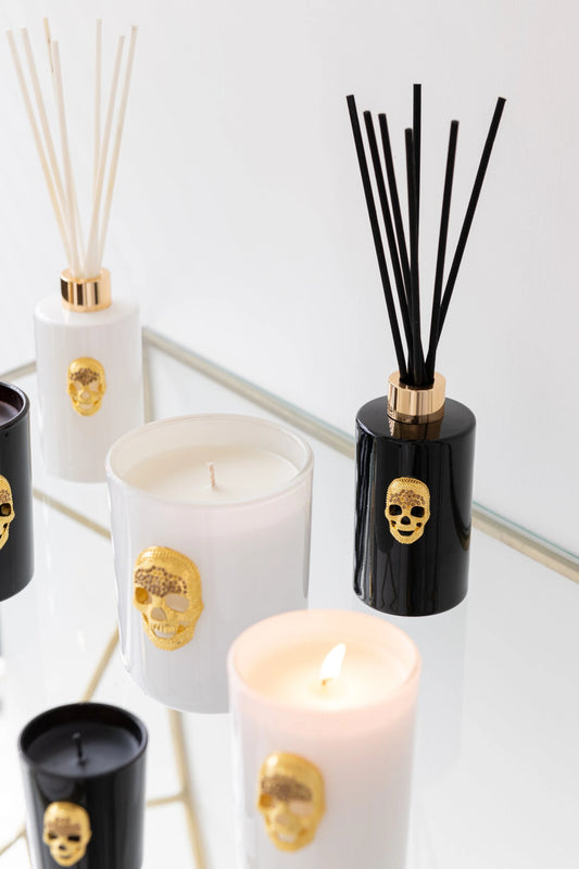Diffusore di fragranza ad asta "Cranio" Nuit Noire firmato Jolipa, caratterizzato da una boccetta cilindrica in vetro nero lucido impreziosita da un dettaglio a rilievo dorato a forma di teschio e un colletto color oro abbinato. Questo esclusivo profumatore d'ambiente di design, completo di bastoncini neri, viene fornito con una raffinata confezione cilindrica coordinata total black con dettagli in oro, ideale per donare un tocco audace, moderno e sofisticato agli interni o come originale idea regalo