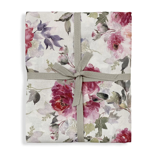 Tovaglia floreale Demetra ripiegata con cura e presentata come confezione regalo, chiusa da un nastro sottile in tessuto grigio annodato con un fiocco centrale. Stampa con grandi peonie colorate.