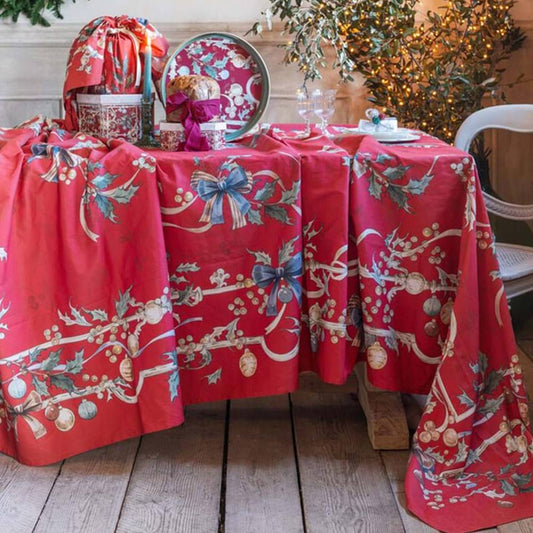 Runner rosso natalizia con decorazioni a tema agrifoglio, fiocchi blu e palline dorate. La tavola è imbandita con panettone, candele e vassoio coordinato in un interno rustico ed elegante.