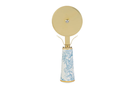 Tagliapizza con decoro azzurro firmato Le Stelle, caratterizzato da una lama rotante circolare in metallo color oro e un elegante manico in porcellana bianca decorato con delicati motivi floreali celestini. Questo raffinato utensile da cucina di design è accompagnato dalla sua custodia regalo rettangolare coordinata con la stessa fantasia botanica, perfetto come bomboniera di classe o idea regalo home decor.