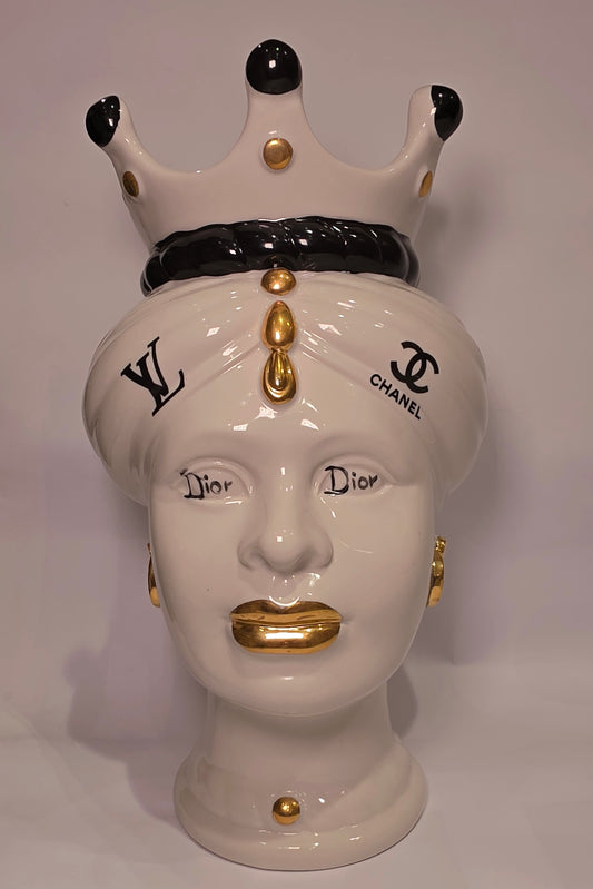 Coppia di Teste di Moro in ceramica bianca lucida con turbanti neri e bianchi decorati da loghi fashion neri e dorati, completate da corone regali e labbra con finitura in oro zecchino. Queste sculture ornamentali di design pop art fondono la tradizione ceramica siciliana con l'estetica del lusso moderno, rappresentando un complemento d'arredo audace ed esclusivo per interni ricercati.