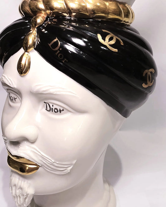 Coppia di Teste di Moro in ceramica bianca lucida con turbanti neri e bianchi decorati da loghi fashion neri e dorati, completate da corone regali e labbra con finitura in oro zecchino. Queste sculture ornamentali di design pop art fondono la tradizione ceramica siciliana con l'estetica del lusso moderno, rappresentando un complemento d'arredo audace ed esclusivo per interni ricercati.