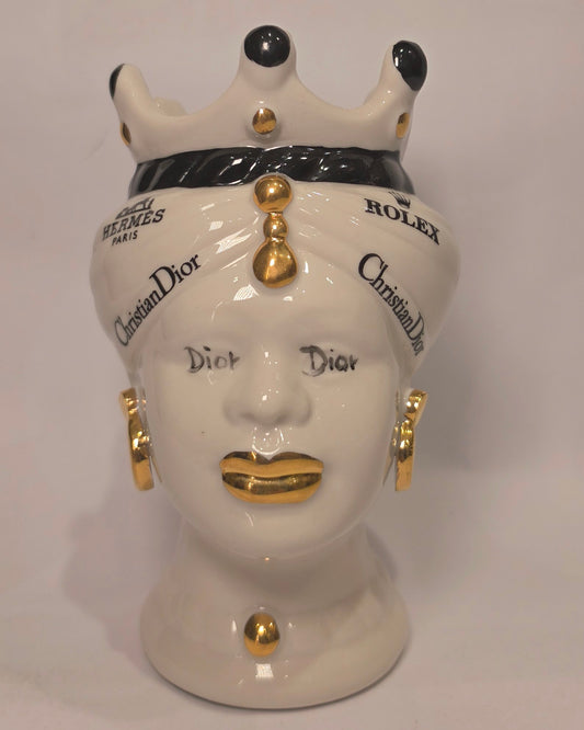 Coppia di Teste di Moro in ceramica bianca lucida con turbanti neri e bianchi decorati da loghi fashion neri e dorati, completate da corone regali e labbra con finitura in oro zecchino. Queste sculture ornamentali di design pop art fondono la tradizione ceramica siciliana con l'estetica del lusso moderno, rappresentando un complemento d'arredo audace ed esclusivo per interni ricercati.