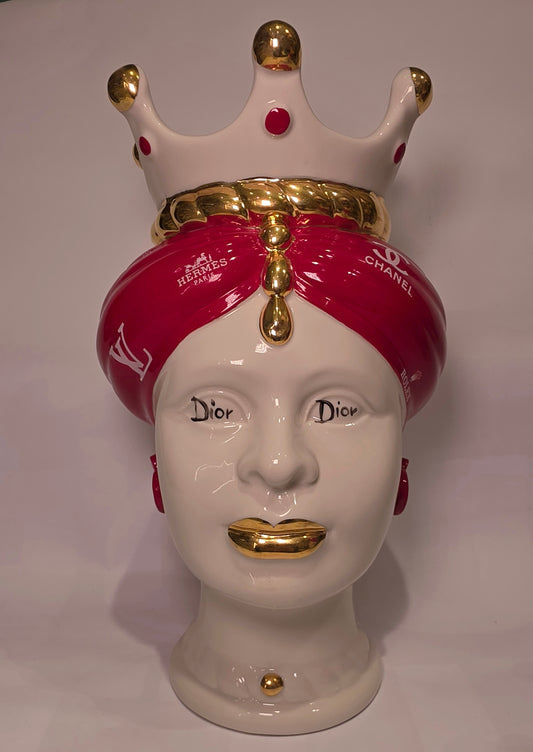 Coppia di Teste di Moro in ceramica bianca lucida con turbanti rosso ciliegia decorati da loghi fashion bianchi, completate da corone regali e labbra con finitura in oro zecchino. Queste sculture ornamentali di design pop art fondono la tradizione ceramica siciliana con l'estetica del lusso moderno, rappresentando un complemento d'arredo audace ed esclusivo per interni ricercati.
