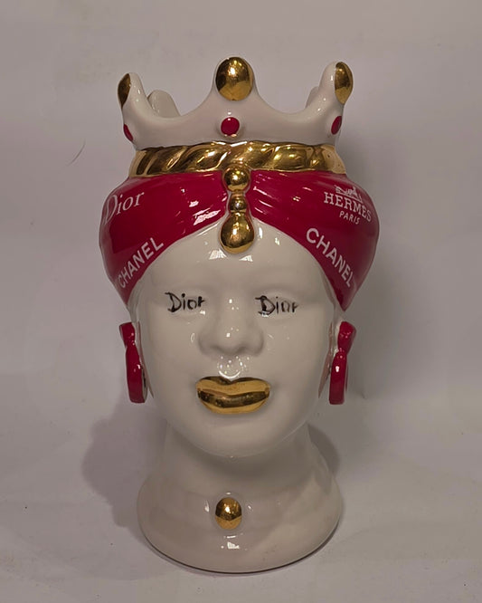 Coppia di Teste di Moro in ceramica bianca lucida con turbanti rosso ciliegia decorati da loghi fashion bianchi, completate da corone regali e labbra con finitura in oro zecchino. Queste sculture ornamentali di design pop art fondono la tradizione ceramica siciliana con l'estetica del lusso moderno, rappresentando un complemento d'arredo audace ed esclusivo per interni ricercati.