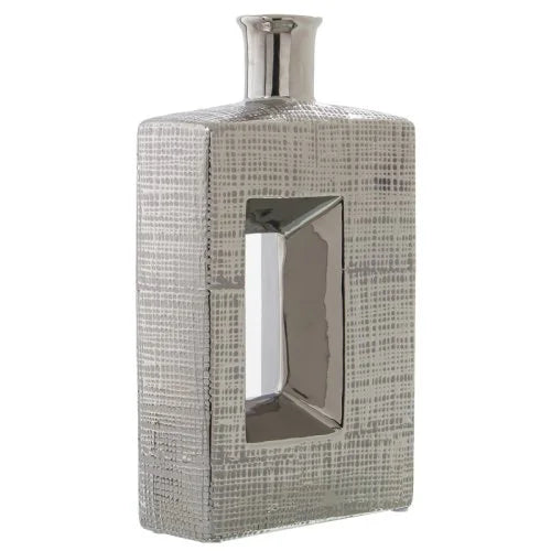Vaso a bottiglia rettangolare verticale firmato Camacho, caratterizzato da un'elegante finitura ceramica color argento lucido con una texture a rilievo finemente lavorata e un originale design geometrico con foro centrale vuoto. Questo moderno complemento d'arredo è provvisto di un collo stretto superiore ideale per ospitare singoli steli floreali, perfetto come sofisticato oggetto ornamentale per impreziosire mobili, consolle o tavoli in contesti contemporanei.
