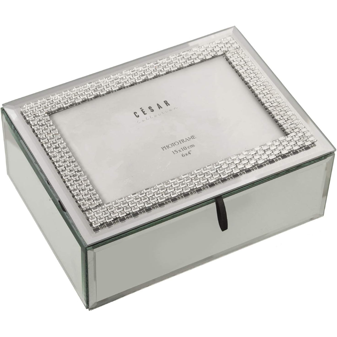 Portagioie rettangolare in vetro specchiato con coperchio a doppia funzione di cornice portafoto, incorniciato da una fascia di brillantini argentati e chiuso da un nastrino nero. Scatola portagioie elegante firmata E-Camacho, ideale come oggetto d'arredo glamour o idea regalo raffinata.