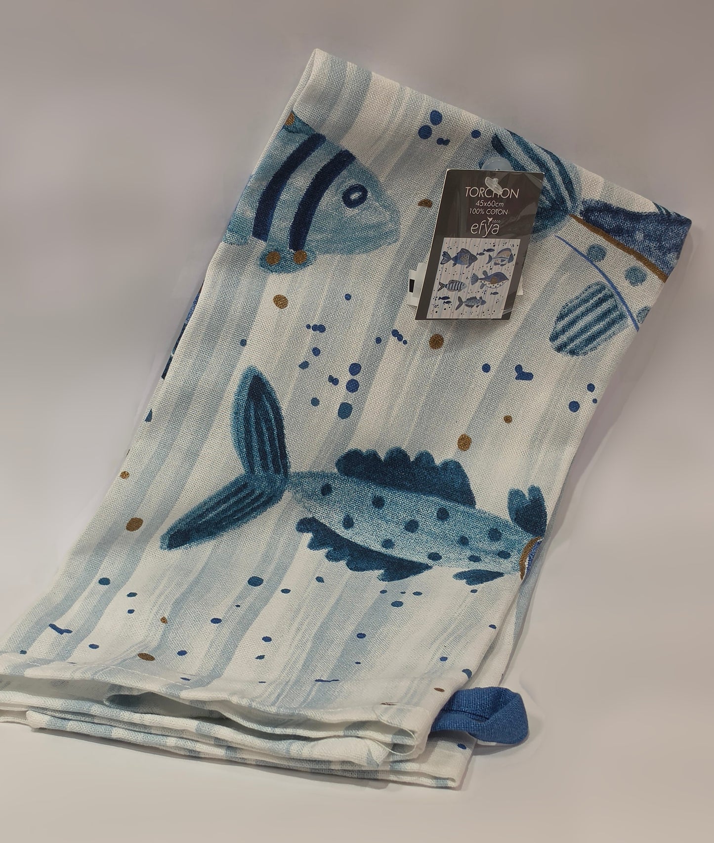 Strofinaccio da cucina in puro cotone del marchio Efya, caratterizzato da una fantasia marina con pesciolini decorativi stampati in varie tonalità di blu e azzurro. Il canovaccio presenta uno sfondo a righe verticali sfumate arricchito da piccoli pois e include una pratica asola blu nell'angolo inferiore per appenderlo comodamente.