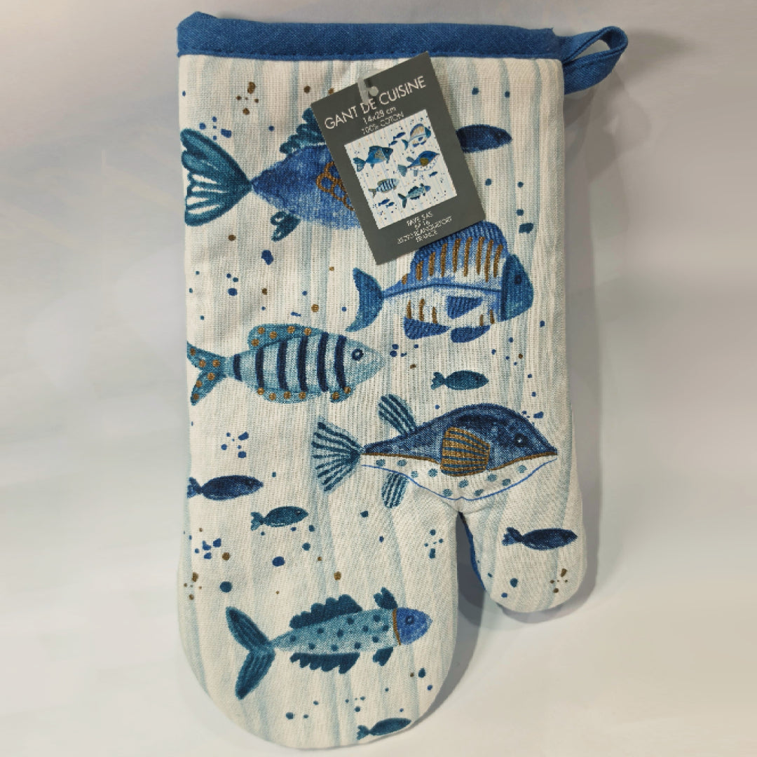 Guantone da cucina in cotone caratterizzato da una fantasia a tema marino con pesciolini stampati in varie tonalità di blu, azzurro e dettagli ocra. Il tessile presenta uno sfondo a righe verticali sfumate e un bordo superiore blu con asola per appenderlo, perfetto per proteggere le mani con stile durante la preparazione dei piatti.