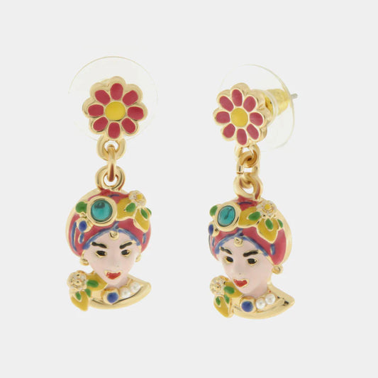 Orecchini pendenti dorati della collezione Etna caratterizzati da un lobo a forma di fiore rosa e giallo e un charm a Testa di Moro finemente smaltato. Il design artigianale presenta dettagli vivaci in rosa, rosso e verde con piccole applicazioni luminose che richiamano la tradizione folk siciliana. Questi orecchini con Testa di Moro rosa e fiori sono l'accessorio perfetto per aggiungere un tocco di colore e cultura mediterranea a un outfit moderno e originale.