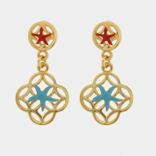 Questi orecchini pendenti dorati della collezione Fiori di Lava si distinguono per il doppio motivo marino con stelle marine smaltate in rosso sul lobo e in azzurro sul pendente principale. La struttura a maiolica traforata in metallo lucido incornicia delicatamente la stella marina centrale, creando un contrasto cromatico vivace e ricercato. Ideali per un outfit estivo, questi orecchini con stelle marine rosse e azzurre rappresentano perfettamente lo stile mediterraneo artigianale di bysimon.
