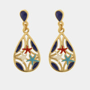 Questi orecchini a goccia della collezione Fiori di Lava presentano un raffinato design traforato in metallo dorato impreziosito da smalti colorati. Il pendente a forma di goccia racchiude tre piccole stelle marine nei toni del rosso, turchese e bianco, completate da eleganti dettagli blu scuro. Caratterizzati da una monachella a lobo con pietra blu, questi orecchini colorati a tema marino offrono uno stile estivo e sofisticato ideale per ogni occasione.