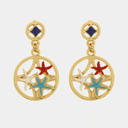 Questi orecchini pendenti dorati della collezione Fiori di Lava presentano un design circolare traforato arricchito da delicate stelle marine smaltate nei toni del rosso, turchese e bianco. Il lobo a bottone decorato con un inserto blu scuro completa la struttura, offrendo un accessorio che unisce l'ispirazione mediterranea a una raffinata vivacità estiva. Questi orecchini con stelle marine colorate sono il tocco perfetto per impreziosire il volto con uno stile artigianale unico e distintivo.