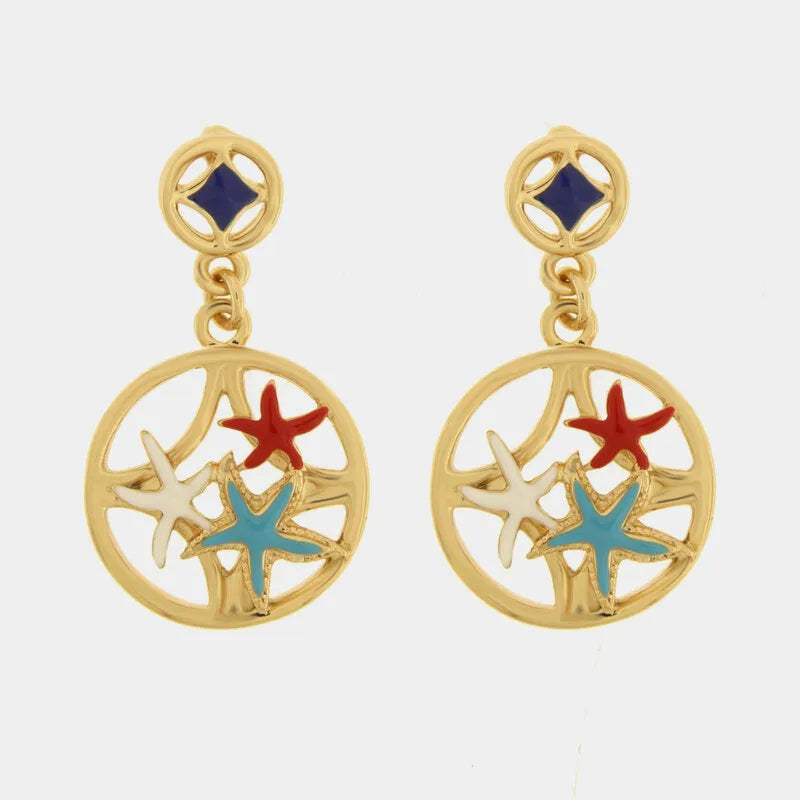 Questi orecchini pendenti dorati della collezione Fiori di Lava presentano un design circolare traforato arricchito da delicate stelle marine smaltate nei toni del rosso, turchese e bianco. Il lobo a bottone decorato con un inserto blu scuro completa la struttura, offrendo un accessorio che unisce l'ispirazione mediterranea a una raffinata vivacità estiva. Questi orecchini con stelle marine colorate sono il tocco perfetto per impreziosire il volto con uno stile artigianale unico e distintivo.