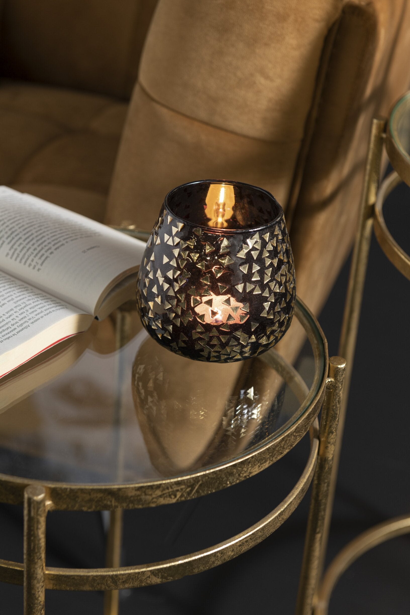 Portacandele decorativo in vetro nero semitrasparente caratterizzato da una raffinata trama geometrica a piccoli triangoli dorati che rivestono l'intera superficie bombata. Questo elegante bicchiere portacandela lascia trasparire una luce calda e soffusa, rendendolo un complemento d'arredo di design ideale per creare un'atmosfera accogliente in casa.