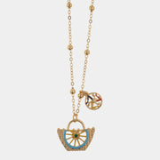 Collana BySimon della collezione Etna con catena dorata a boules, pendente a forma di borsetta intrecciata con ruota del carretto smaltata celeste e charm laterale della Trinacria.