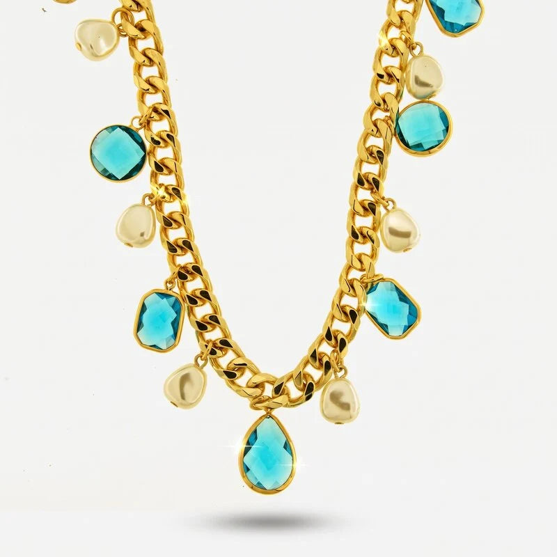 Collana a catena dorata con cristalli sfaccettati color celeste in forme variegate e perle barocche pendenti. Gioiello scenografico dal forte impatto visivo, ideale per occasioni speciali e come idea regalo.