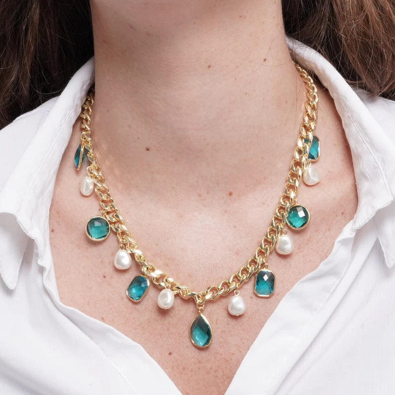 Collana a catena dorata con cristalli sfaccettati color celeste in forme variegate e perle barocche pendenti. Gioiello scenografico dal forte impatto visivo, ideale per occasioni speciali e come idea regalo.