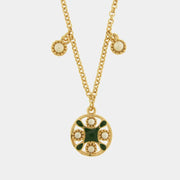 Collana in metallo con finitura dorata del marchio BySimon appartenente alla collezione Fiori di Lava caratterizzata da una catenina sottile a maglia rolo che sostiene un pendente circolare traforato ispirato alle maioliche mediterranee. Il ciondolo principale presenta un decoro centrale a croce in smalto verde scuro circondato da quattro perle bianche incastonate in una cornice dorata lavorata a sbalzo. Lungo la catena sono presenti due ulteriori piccole perle bianche decorative che scendono simmetricament