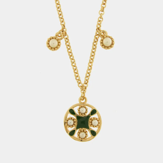 Collana in metallo con finitura dorata del marchio BySimon appartenente alla collezione Fiori di Lava caratterizzata da una catenina sottile a maglia rolo che sostiene un pendente circolare traforato ispirato alle maioliche mediterranee. Il ciondolo principale presenta un decoro centrale a croce in smalto verde scuro circondato da quattro perle bianche incastonate in una cornice dorata lavorata a sbalzo. Lungo la catena sono presenti due ulteriori piccole perle bianche decorative che scendono simmetricament