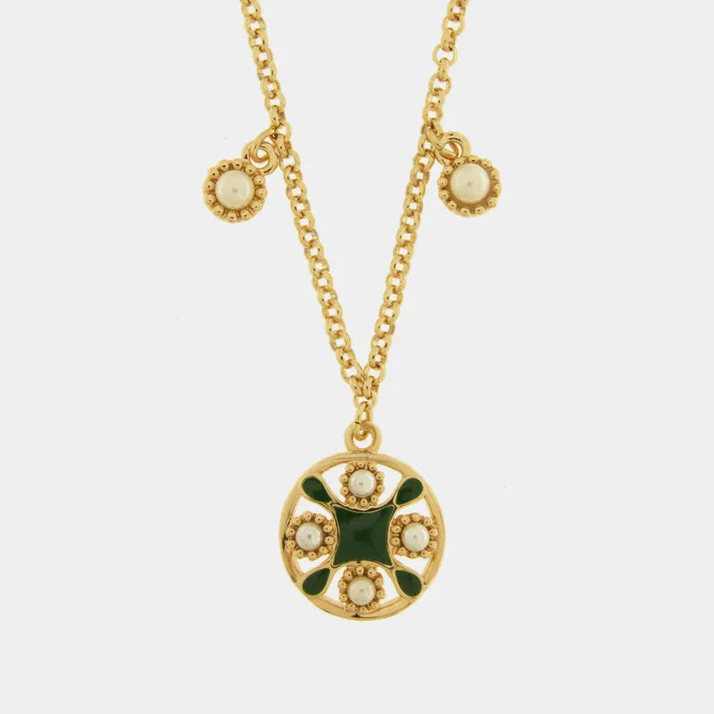 Collana in metallo con finitura dorata del marchio BySimon appartenente alla collezione Fiori di Lava caratterizzata da una catenina sottile a maglia rolo che sostiene un pendente circolare traforato ispirato alle maioliche mediterranee. Il ciondolo principale presenta un decoro centrale a croce in smalto verde scuro circondato da quattro perle bianche incastonate in una cornice dorata lavorata a sbalzo. Lungo la catena sono presenti due ulteriori piccole perle bianche decorative che scendono simmetricament