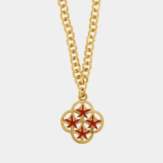 Una collana a catena dorata con un ciondolo pendente quadrilobato traforato è presentata su uno sfondo bianco neutro. Il ciondolo dorato è decorato con quattro elementi a forma di stella marina di colore rosso brillante disposti simmetricamente. Questo gioiello appartiene alla collezione Fiori di Lava  del marchio bysimon