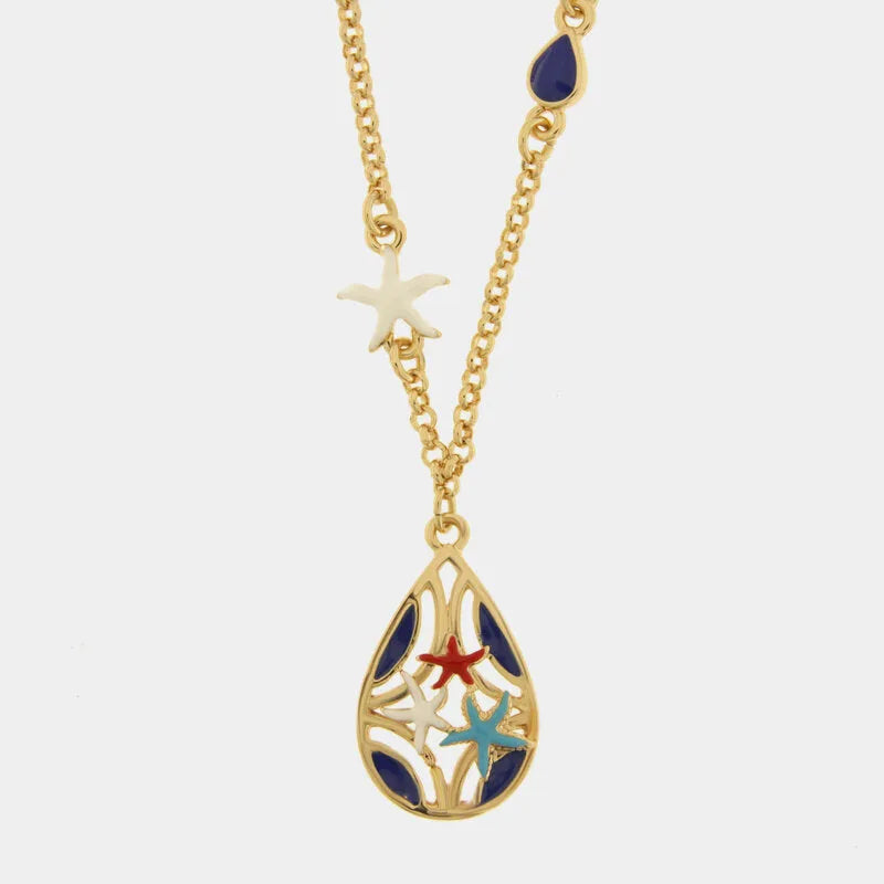 Collana in metallo con finitura dorata del marchio BySimon appartenente alla collezione Fiori di Lava caratterizzata da una catenina a maglia rolo che sostiene un pendente a forma di goccia con lavorazione traforata a trama floreale. Il ciondolo è decorato con sette stelle marine tridimensionali smaltate, di cui sei di colore rosso vibrante posizionate lungo il bordo e una centrale di colore azzurro a contrasto. La collana è impreziosita lateralmente da due piccole perle bianche incastonate lungo la catena,