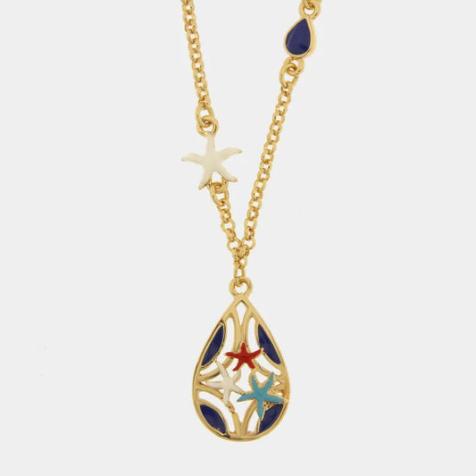 Collana in metallo con finitura dorata del marchio BySimon appartenente alla collezione Fiori di Lava caratterizzata da una catenina a maglia rolo che sostiene un pendente a forma di goccia con lavorazione traforata a trama floreale. Il ciondolo è decorato con sette stelle marine tridimensionali smaltate, di cui sei di colore rosso vibrante posizionate lungo il bordo e una centrale di colore azzurro a contrasto. La collana è impreziosita lateralmente da due piccole perle bianche incastonate lungo la catena,